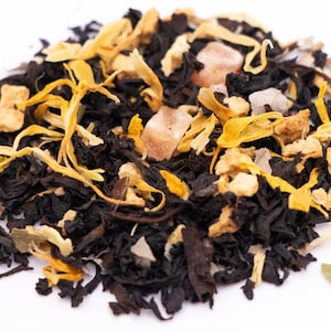 May include: A close-up of a blend of black tea leaves, dried fruit pieces, and sugar crystals. The tea blend is a mix of black tea, dried mango, and sugar crystals.