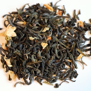May include: A close-up of a pile of loose leaf green tea with dried orange peel and flower petals.