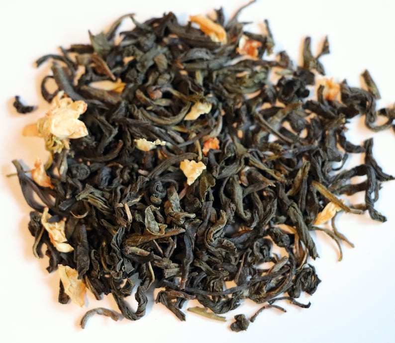 May include: A close-up of a pile of loose leaf green tea with dried orange peel and flower petals.
