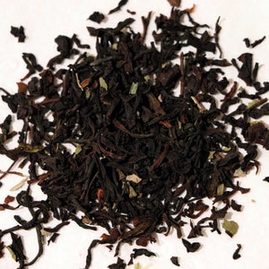 May include: A close-up of a pile of loose leaf black tea with green tea leaves and stems. The tea is dark brown and black in color.