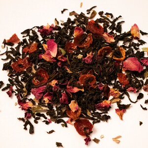 May include: A close-up of a blend of black tea leaves, dried rose petals, and dried fruit pieces. The tea blend is a mix of dark brown, red, and orange colors.