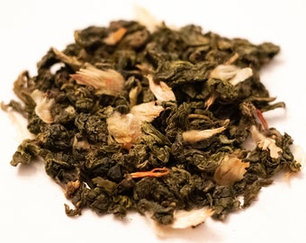 May include: A close-up of a pile of loose leaf green tea with white and orange flower petals.