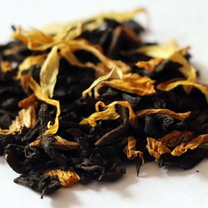 May include: A close-up of a blend of black tea leaves and dried orange peel. The tea leaves are dark brown and the orange peel is a bright orange.