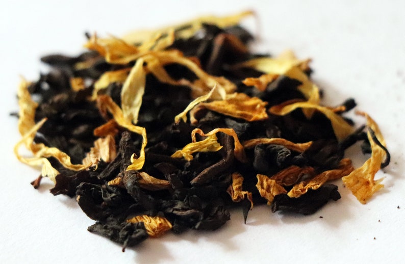 May include: A close-up of a blend of black tea leaves and dried orange peel. The tea leaves are dark brown and the orange peel is a bright orange.