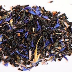 May include: A close-up of a blend of black tea leaves with blue cornflower petals and yellow pieces of fruit.