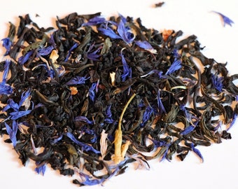 May include: A close-up of a blend of black tea leaves with blue cornflower petals and yellow pieces of fruit.