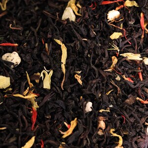 Pu&ograve; includere: Primo piano di foglie di t&egrave; nero con pezzi di frutta e petali di fiori di colore arancione, bianco e rosso.
