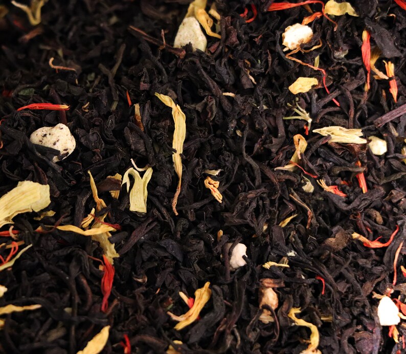 Pu&ograve; includere: Primo piano di foglie di t&egrave; nero con pezzi di frutta e petali di fiori di colore arancione, bianco e rosso.