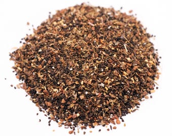 May include: A close-up shot of a pile of loose-leaf tea. The tea is a mix of dark brown, black, and tan pieces, with visible herbs and spices. The tea is on a white background.