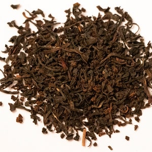 May include: A close-up of a pile of loose leaf black tea. The tea leaves are dark brown and have a slightly curled shape.