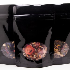 May include: Three black stand-up pouches with clear view windows. Each pouch contains a different blend of dried tea leaves and flowers.