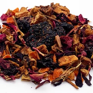 May include: A close-up of a pile of loose leaf tea. The tea blend features a mix of dried fruits, flowers, and herbs in shades of red, orange, brown, and black. The tea is scattered on a white surface.