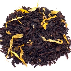 May include: Close-up of loose leaf tea with dark brown leaves and yellow flower petals. The tea leaves are tightly packed together, with the yellow petals scattered throughout. The tea is likely a black tea blend.