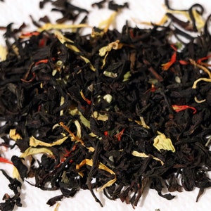 Pu&ograve; includere: Primo piano di un blend di foglie di t&egrave; nero con scorza d'arancia secca, petali di ibisco rossi e foglie di t&egrave; verde.