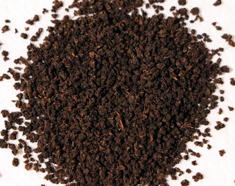 May include: Close-up of a pile of loose leaf black tea. The tea leaves are dark brown and appear to be broken into small pieces.