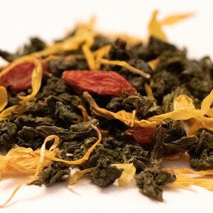 May include: Close-up of a blend of loose leaf tea with green tea leaves, dried goji berries, and yellow flower petals.