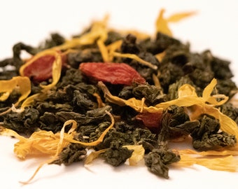 May include: Close-up of a blend of loose leaf tea with green tea leaves, dried goji berries, and yellow flower petals.