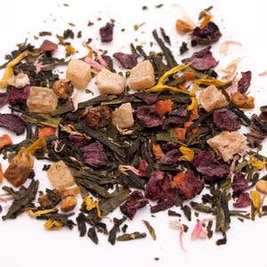 May include: A mix of green tea leaves, dried fruit pieces, and candied fruit. The fruit pieces are in shades of red, orange, and yellow.