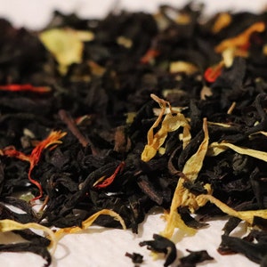 Pu&ograve; includere: Primo piano di un blend di foglie di t&egrave; nero con petali di fiori arancioni, gialli e rossi.