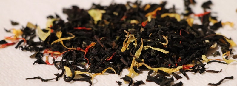 Pu&ograve; includere: Primo piano di un blend di foglie di t&egrave; nero con petali di fiori arancioni, gialli e rossi.