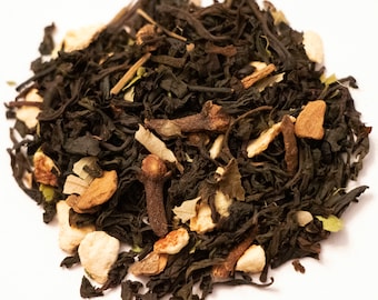 May include: Close-up of loose-leaf tea blend with dark tea leaves, cloves, and pieces of dried fruit. The tea blend has a variety of textures and colors, including dark brown, tan, and light brown. The tea is scattered on a white surface.