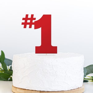 May include: Red number one cake topper with a hashtag symbol. The topper is on top of a white frosted cake.