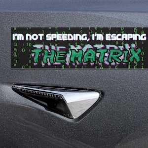 Puede incluir: Adhesivo negro en un coche gris con el texto "I'M NOT SPEEDING, I'M ESCAPING THE MATRIX" en blanco y verde. La pegatina tiene un diseño digital y glitch.