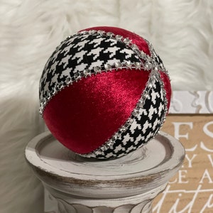 May include: A red and black Christmas ornament with a houndstooth pattern and silver rhinestones. The ornament is sitting on a white pedestal.
