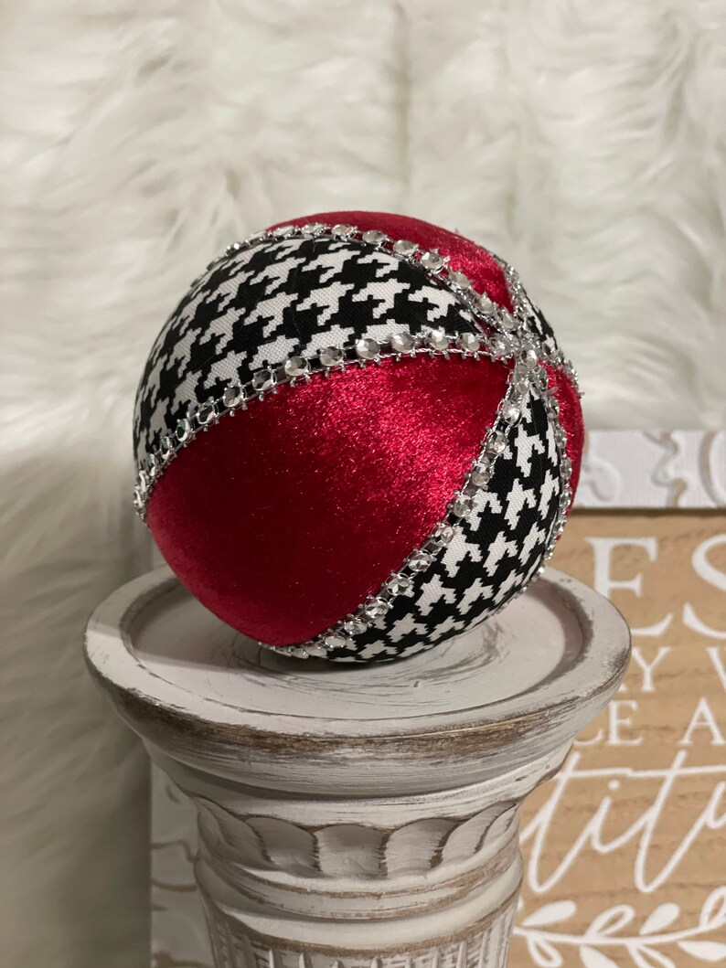 May include: A red and black Christmas ornament with a houndstooth pattern and silver rhinestones. The ornament is sitting on a white pedestal.