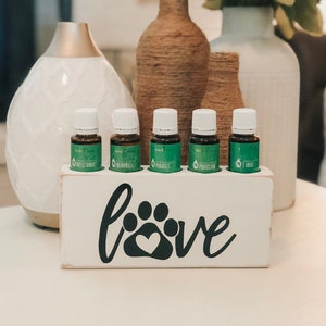 Può includere: Scatola di legno bianca con la parola "love" e un'impronta di zampa con un cuore al centro. La scatola contiene cinque piccoli flaconi di vetro con liquido verde e etichette che recitano "Infect Away", "Mendowell", "Purify", "Purisclean" e "T-Away".