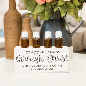 May include: White wooden essential oil holder with four amber glass bottles. The holder has the text "I can do all things through Christ who strengthens me Philippians 4:13" printed on it.
