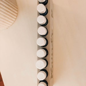 May include: A white wooden essential oil rack with the word "remarkable" printed on it. The rack holds ten small glass bottles with white caps.
