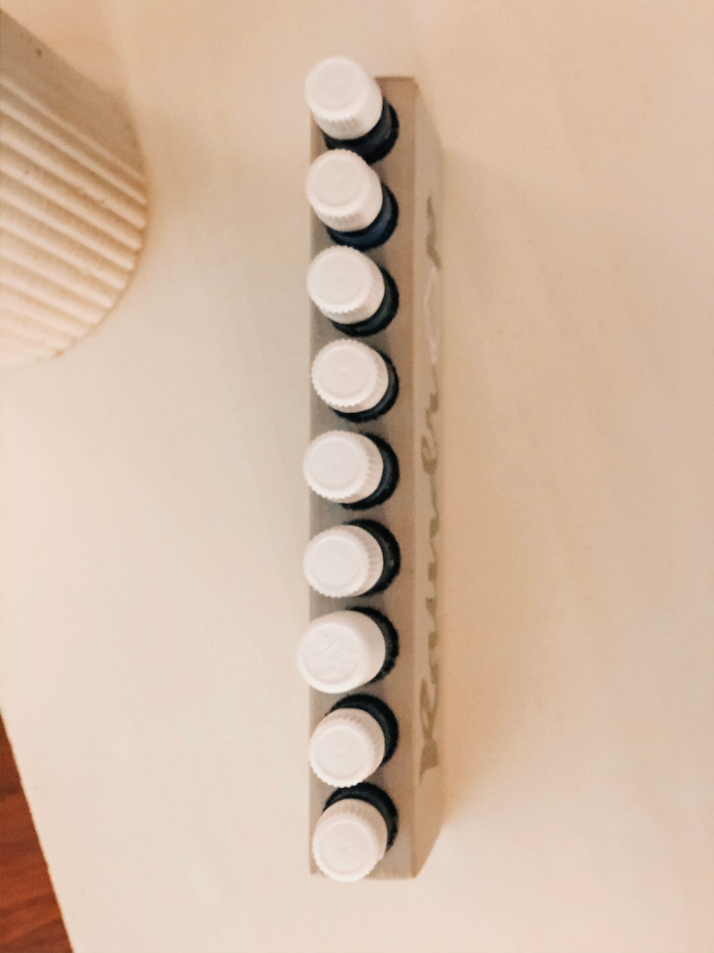May include: A white wooden essential oil rack with the word "remarkable" printed on it. The rack holds ten small glass bottles with white caps.