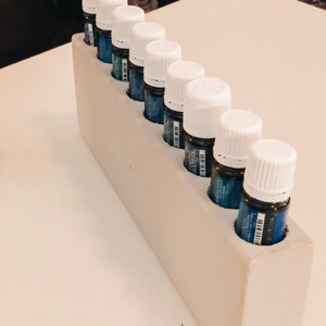 May include: A white wooden rack with eight small white bottles with blue liquid inside. The bottles are arranged in a row, with the caps facing the viewer.