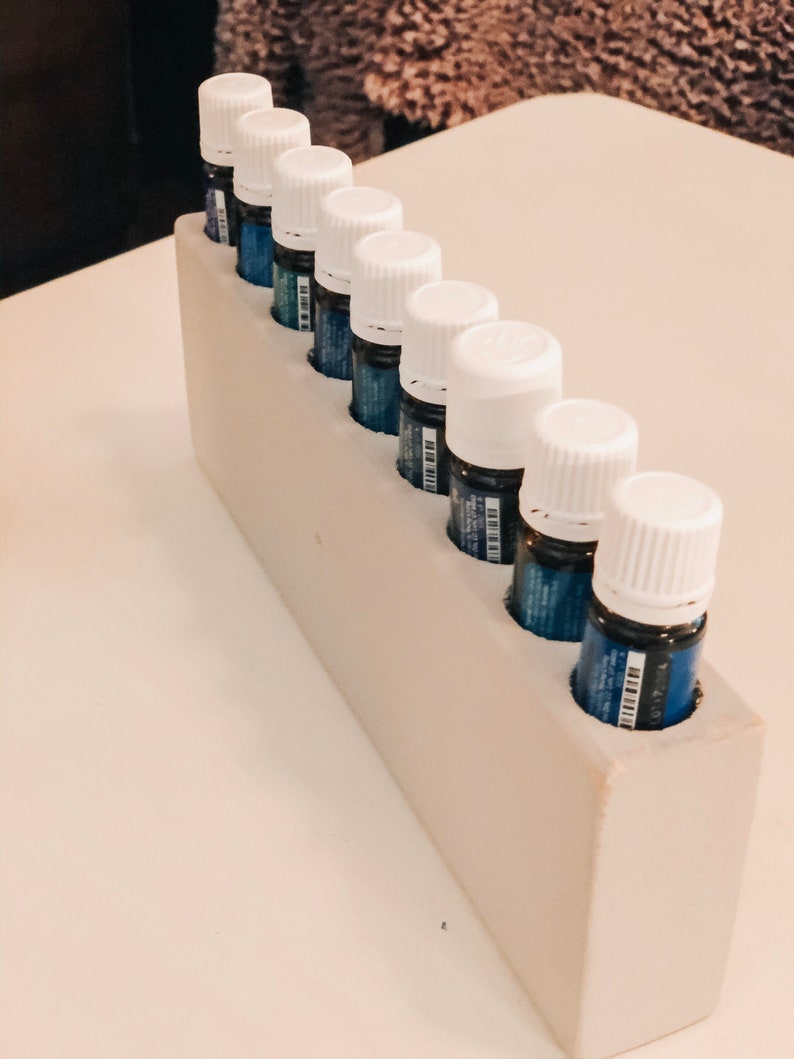 May include: A white wooden rack with eight small white bottles with blue liquid inside. The bottles are arranged in a row, with the caps facing the viewer.