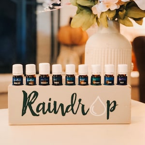 May include: A wooden box with the word "Raindrop" and a white raindrop graphic. The box holds 10 small glass bottles with blue and green liquid.