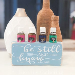 May include: A light blue wooden box with the words "be still and know" and "Psalm 46:10" in white lettering. The box has four slots for essential oil bottles, which are labelled "Joy", "Bergamot", "Juniper", and "Peace & Calming".