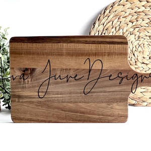 Könnte beinhalten: Ein Schneidebrett aus Holz mit einem Griff, auf dem der Text "Ava June Designs" in einer kursivschriftlichen Schriftart steht.