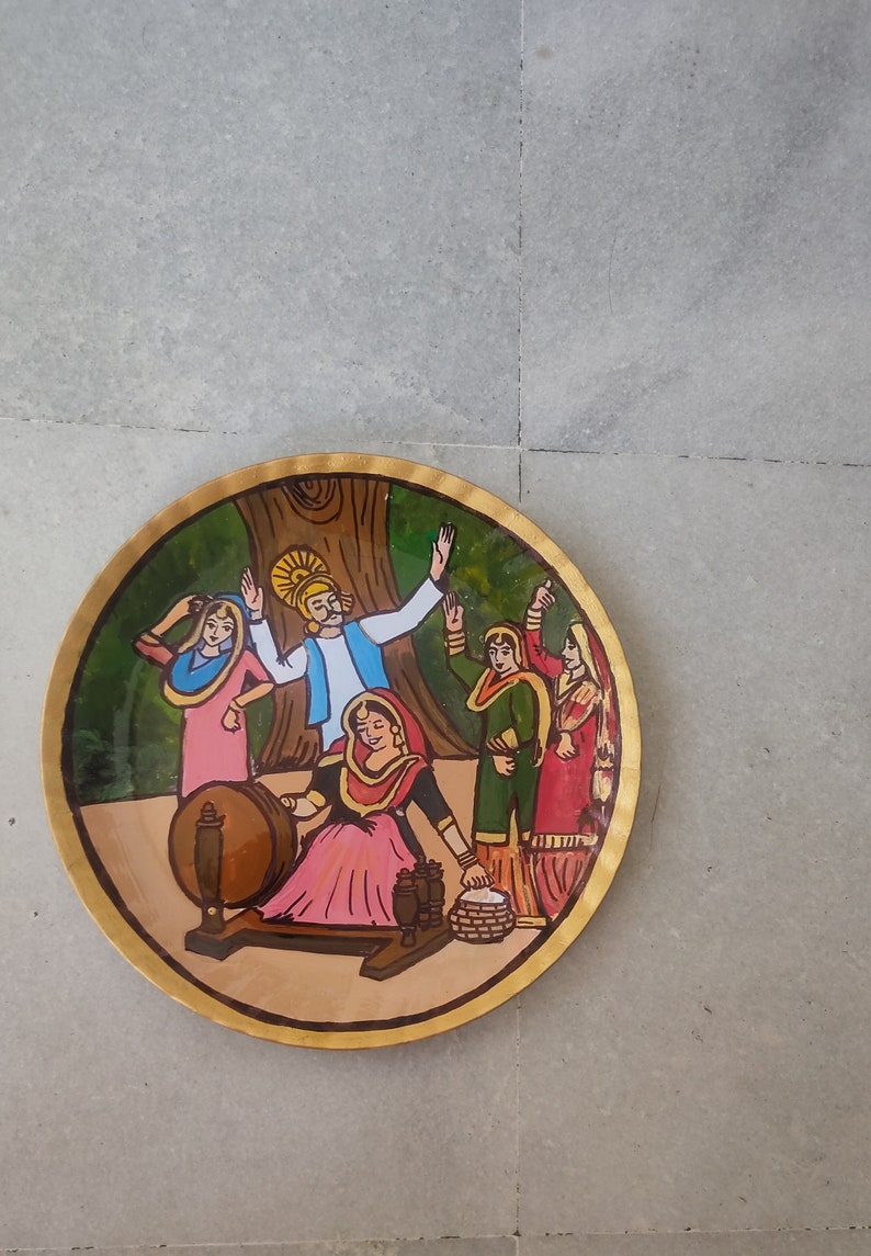 K&ouml;nnte beinhalten: Ein runder Holzteller mit einer bemalten Szene von Menschen in traditioneller Kleidung. Die Szene zeigt eine Frau, die Wolle an einem Spinnrad spinnt, einen Mann mit einem gelben Turban und zwei Frauen in bunten Kleidern. Der Teller hat einen goldenen Rand.