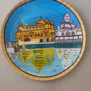 K&ouml;nnte beinhalten: Ein handbemalter runder Teller, der einen goldenen Tempel mit blauem Himmel und Wasserreflexion zeigt. Der Tempel hat eine goldene Kuppel und komplizierte Details. Der Teller hat einen goldenen Rand.
