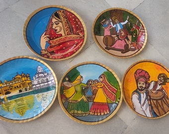 May include: Five round decorative plates with painted scenes of Indian culture. The plates feature a woman in a red veil, a group of people dancing, a golden temple, a couple dancing, and two men playing a drum.