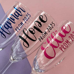 May include: Three champagne flutes with personalised names and the text "Prom 2025". The flutes are decorated with blue, black, and pink lettering.
