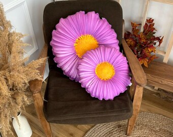 May include: Two purple and yellow floral throw pillows with a daisy design on a brown armchair.