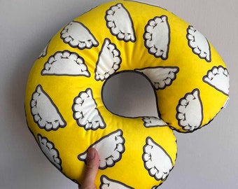 May include: A yellow donut-shaped pillow with a white and gray print of dumplings. The pillow is soft and comfortable and would be great for sleeping or lounging.