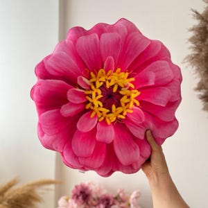 May include: A pink and yellow flower pillow with a round shape. The pillow is made of fabric and has a realistic flower design.