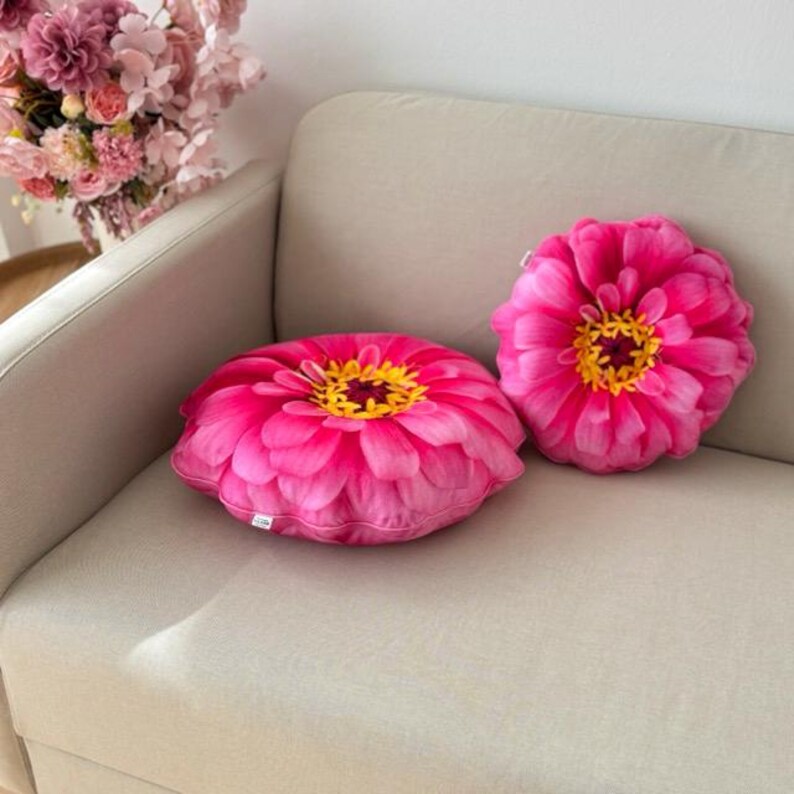 May include: Two pink flower-shaped throw pillows with yellow centers on a white couch.