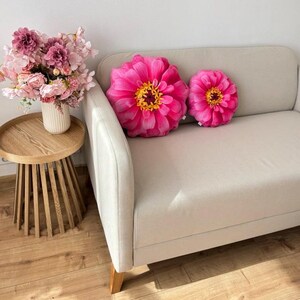May include: Two pink and yellow floral throw pillows with a large flower design on a light gray couch.
