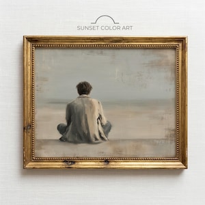 Puede incluir: Una obra de arte enmarcada titulada "Sunset Color Art" representa a una persona sentada en una playa, de espaldas al espectador. La pintura presenta tonos apagados de gris, beige y dorado, con una estética vintage. El marco es ornamentado.
