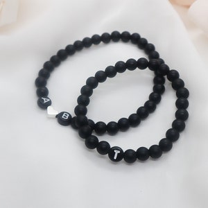 May include: Two black beaded bracelets with silver heart and letter charms. The bracelets spell out "AB" and "T".