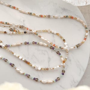 May include: Three layered necklaces with white pearls and various colored beads, including green, brown, orange, and purple.